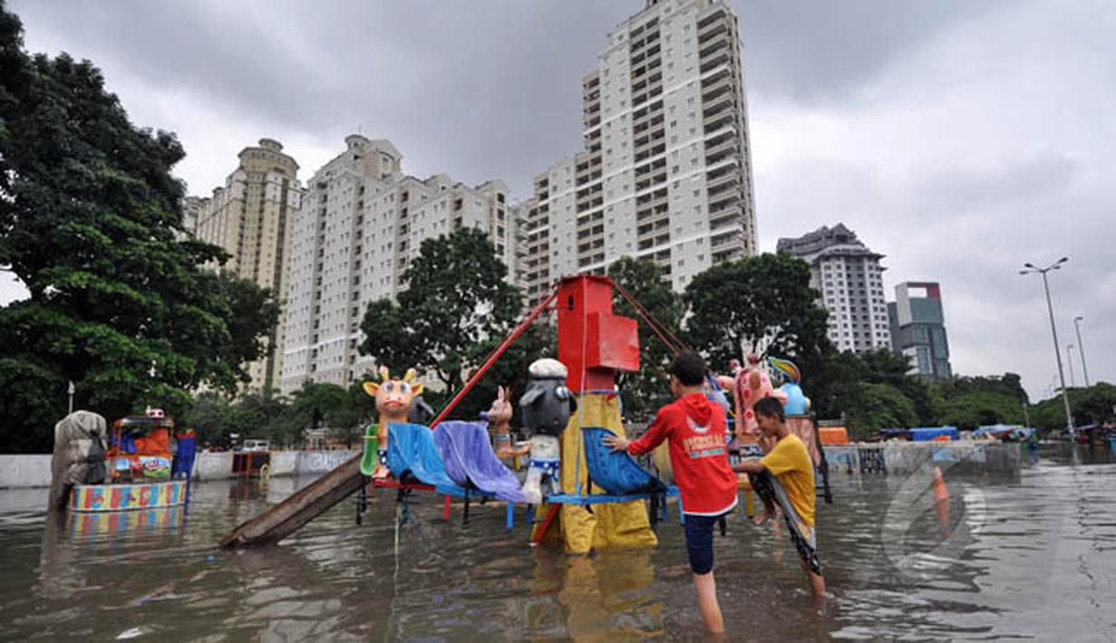 Sejumlah anak bermain di lahan bermain Kemayoran yang terendam banjir, Jakarta, Selasa (10/2). Tingginya curah hujan di wilayah Jakarta mengakibatkan sejumlah daerah masih terendam banjir. (Liputan6.com/Faizal Fanani)