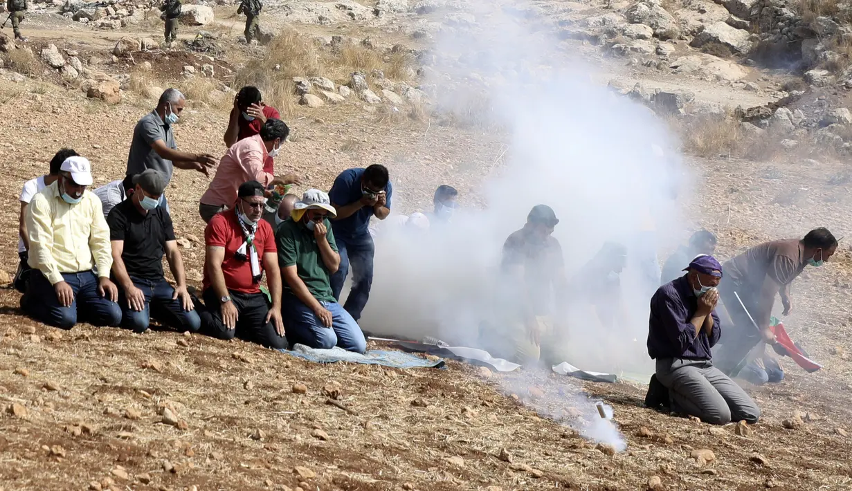 Pengunjuk rasa Palestina melaksanakan salat di tengah tembakan gas air mata tentara Israel di dekat desa Beit Dajan, Palestina (9/10/2020). Insiden terjadi ketika pengunjuk rasa menggelar aksi memprotes pencaplokan tanah yang dilakukan Israel untuk perluasan permukiman Yahudi. (AFP/Jaafar Ashtiyeh)