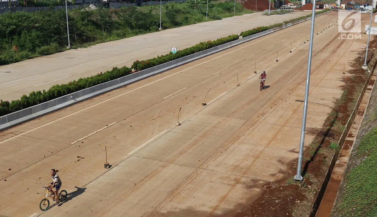 Warga bersepeda di proyek Jalan Tol Cijago Seksi II, kawasan Kukusan, Depok, Minggu (6/1). Proyek yang hampir rampung itu dimanfaatkan untuk berolahraga dengan menyusuri jalur yang belum dilalui kendaraan bermotor. (Liputan6.com/Immanuel Antonius)