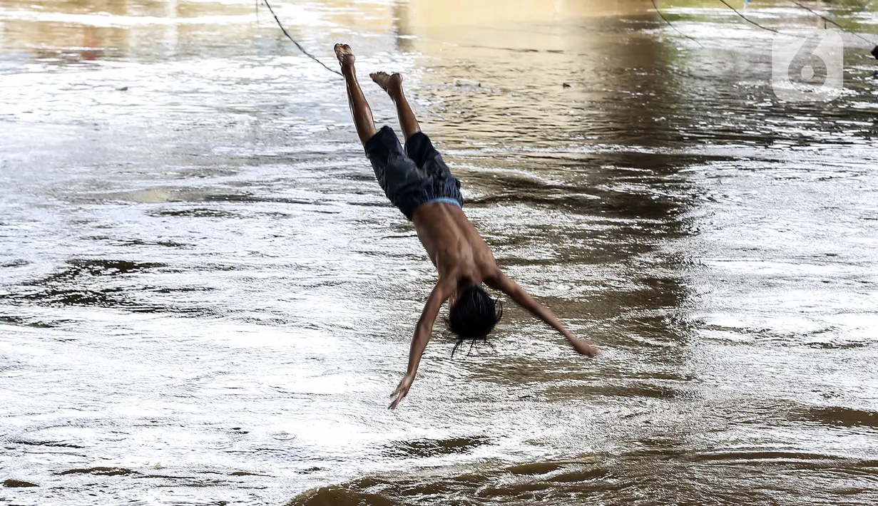 Seorang anak melompat ke Sungai Ciliwung saat banjir melanda Jalan Bina Warga Rt 005/Rw 07 Kelurahan Rawa Jati, Jakarta, Senin (8/2/2021). Banjir setinggi 60-190 cm tersebut disebabkan oleh luapan air Sungai Ciliwung dan curah hujan Jakarta yang tinggi. (Liputan6.com/Johan Tallo)