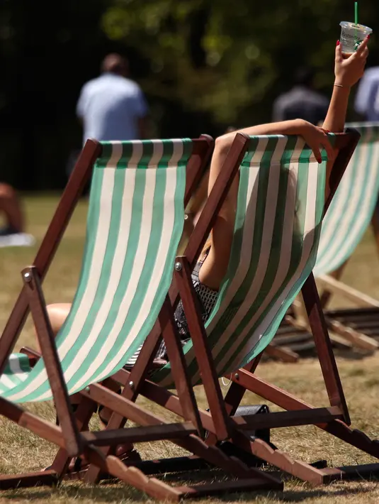 Warga Inggris bersantai di atas kursi sambil menikmati sinar matahari di St James's Park, London, Senin (25/6). Pada Juli 2018, suhu di ibu kota London tercatat 29.1 derajat Celcius dan diprediksi akan mencapai 30 derajat Celcius. (Yui Mok/PA via AP)