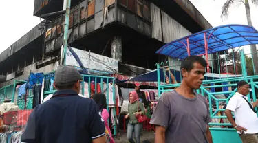 Pengunjung melewati pedagang korban kebakaran yang berjualan di area parkir Pasar Senen, Jakarta, Rabu (8/2). Belum tersedianya tempat penampungan sementara membuat para pedagang terpaksa mendirikan tenda lapak. (Liputan6.com/Immanuel Antonius)
