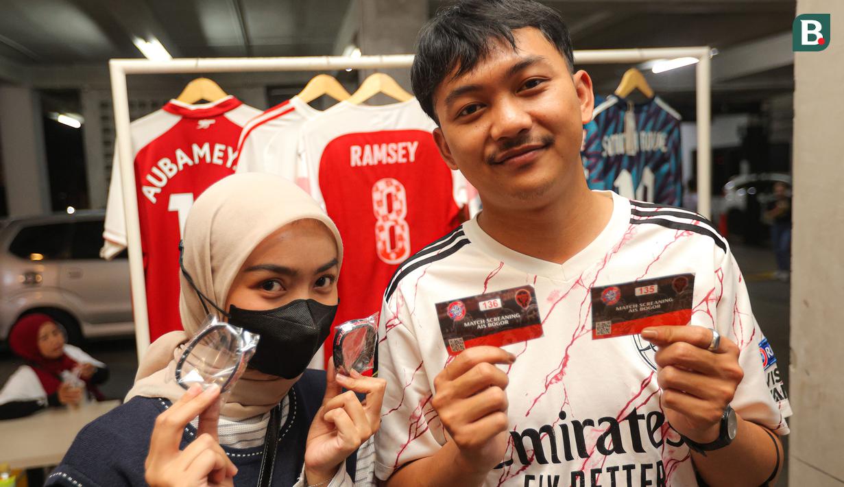 Dua orang peserta memperlihatkan merchandise yang didapatkan setelah melakukan registrasi Roaring Night pertandingan Liga Inggris 2023/2024 antara Arsenal kontra Crystal Palace yang dilaksanakana berbarengan dengan Gathering Nasional Arsenal Indonesia Supporters (AIS) di Bucketlist Indonesia, Bogor, Sabtu (20/1/2024). (Bola.com/Bagaskara Lazuardi)