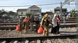 Ibu-ibu menyeberangi perlintasan rel kereta api di kawasan Pisangan Baru, Jakarta, Selasa (10/9/2019). Mereka nekat menantang maut menyeberangi rel di dekat stasiun Jatinegara tersebut lantaran tidak adanya akses jembatan penyeberangan orang (JPO). (merdeka.com/Iqbal Nugroho)