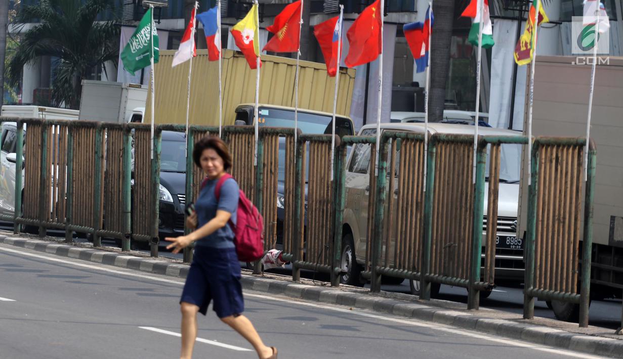 Pejalan kaki menyeberang dekat bendera negara peserta Asian Games 2018 yang diikat di tiang bambu di pagar pembatas Jalan Pluit Selatan Raya, Jakarta, Kamis (19/7). Pemasangan itu inisiatif warga dalam memeriahkan Asian Games. (Liputan6.com/Arya Manggala)