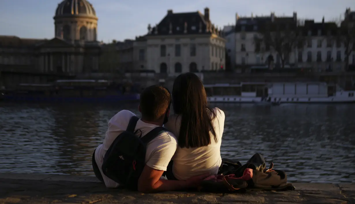 Sepasang kekasih menikmati matahari terbenam di tepi sungai Seine, di Paris (29/3/2021). Sungai ini merupakan salah satu jalur lalu lintas air komersial dan juga menjadi sebuah tujuan wisata, khususnya bagian yang terletak dalam kota Paris. (AP Photo/Thibault Camus)