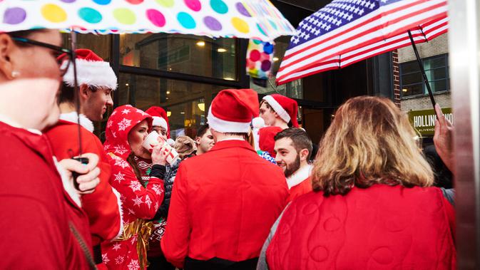 Orang-orang yang berpakaian seperti Sinterklas berdiri di tengah hujan saat berpartisipasi  dalam acara tahunan Santacon di New York City, Sabtu (14/12/2019). Dalam acara tersebut, peserta berkeliling bar untuk menyambut datangnya liburan Natal. (Gabby Jones/Getty Images/AFP)