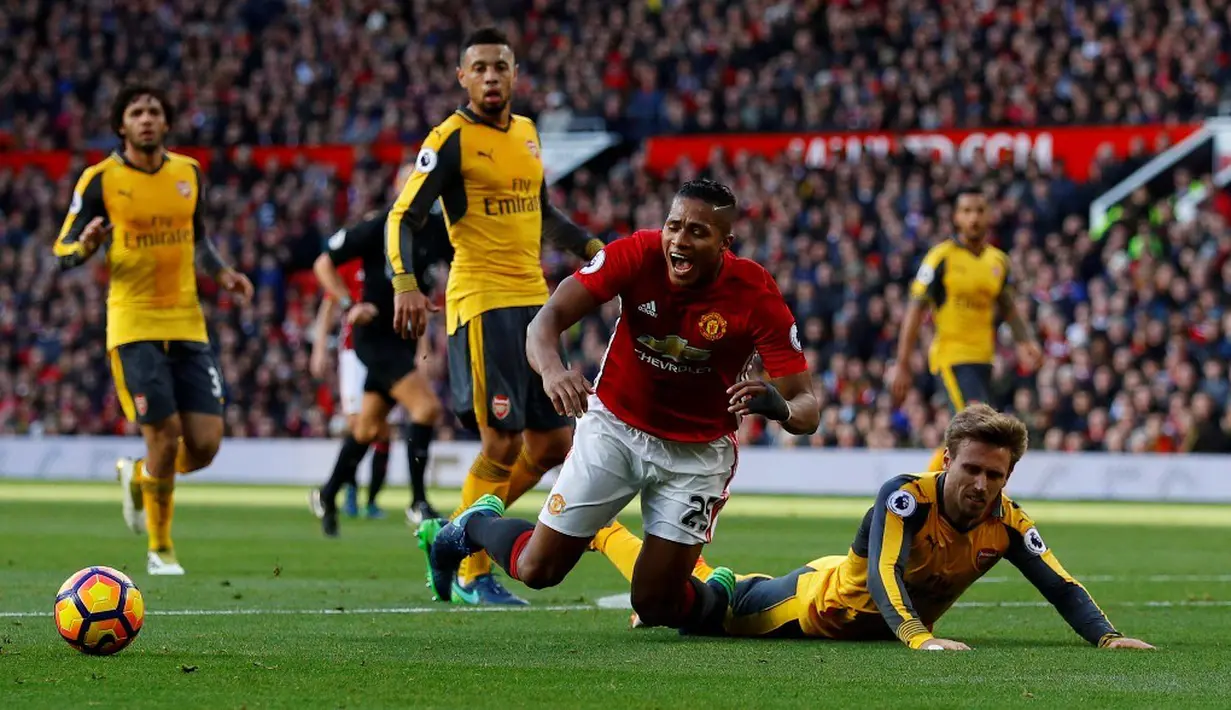 Pemain MU, Antonio Valencia, terjatuh saat berebut bola dengan pemain Arsenal, Nacho Monreal, dalam laga Premier League di Stadion Old Trafford, Sabtu (19/11/2016). (Reuters/Phil Noble)