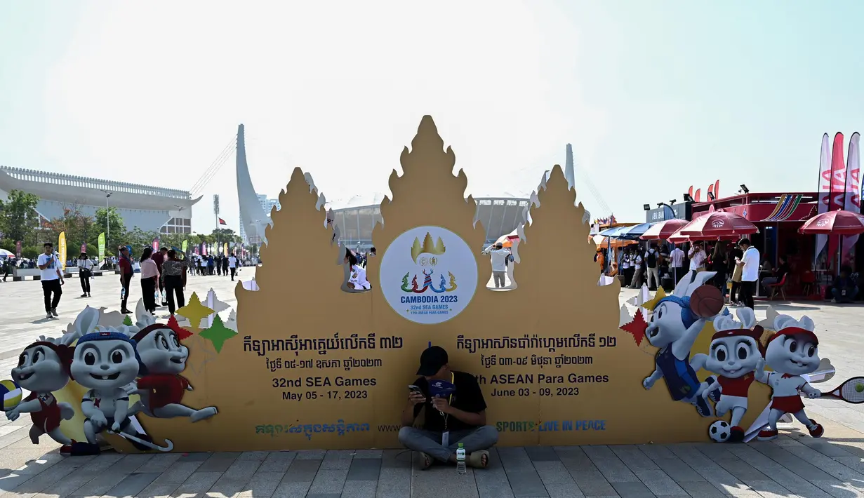 Untuk menghindari sengatan sinar matahari, seorang pria bernaung di bawah naungan papan nama Pesta Olahraga Asia Tenggara (SEA Games) ke-32 di luar Stadion Nasional Morodok Techo menjelang upacara pembukaan acara tersebut di Phnom Penh pada tanggal 5 Mei 2023. (NHAC NGUYEN/AFP)