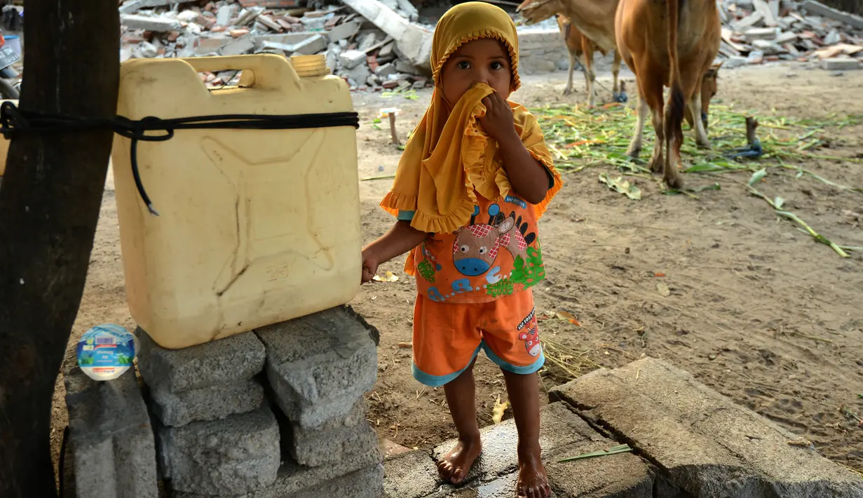 Seorang anak berdiri di depan rumahnya yang rusak akibat gempa di kecamatan Kayangan di Lombok Utara, Rabu (8/8). BPBD Lombok Utara mencatat data sementara jumlah korban jiwa akibat gempa Lombok mencapai 347 orang. (AFP/SONNY TUMBELAKA)