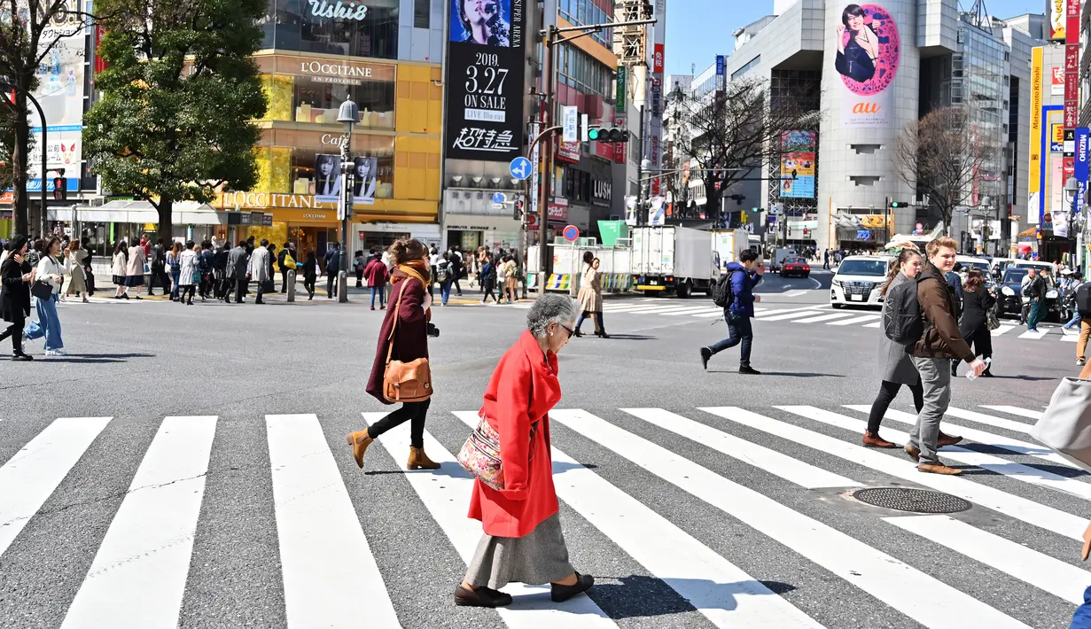 Pejalan kaki melintasi persimpangan pejalan kaki yang terkenal di distrik Shibuya, Tokyo pada 20 Maret 2019. Persimpangan jalan ini menjadi salah satu persimpangan terbesar dan tersibuk di dunia. (Photo by CHARLY TRIBALLEAU / AFP)