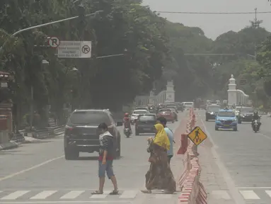 Orang-orang menyeberang jalan yang tertutup abu setelah letusan Gunung Merapi di Solo (3/3/2020). Gunung paling aktif di Indonesia tersebut meletus pada 3 Maret pukul 05.22 WIB dengan tinggi kolom 6.000 meter. (AFP Photo/Dika)