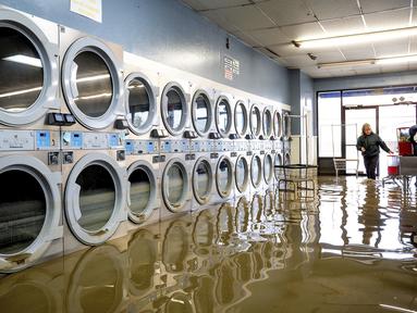Pamela Cerruti berjalan melewati Pajaro Coin Laundry saat banjir mengelilingi mesin-mesin di komunitas Pajaro di Monterey County, California, Selasa, 14 Maret 2023.  (AP Photo/Noah Berger)