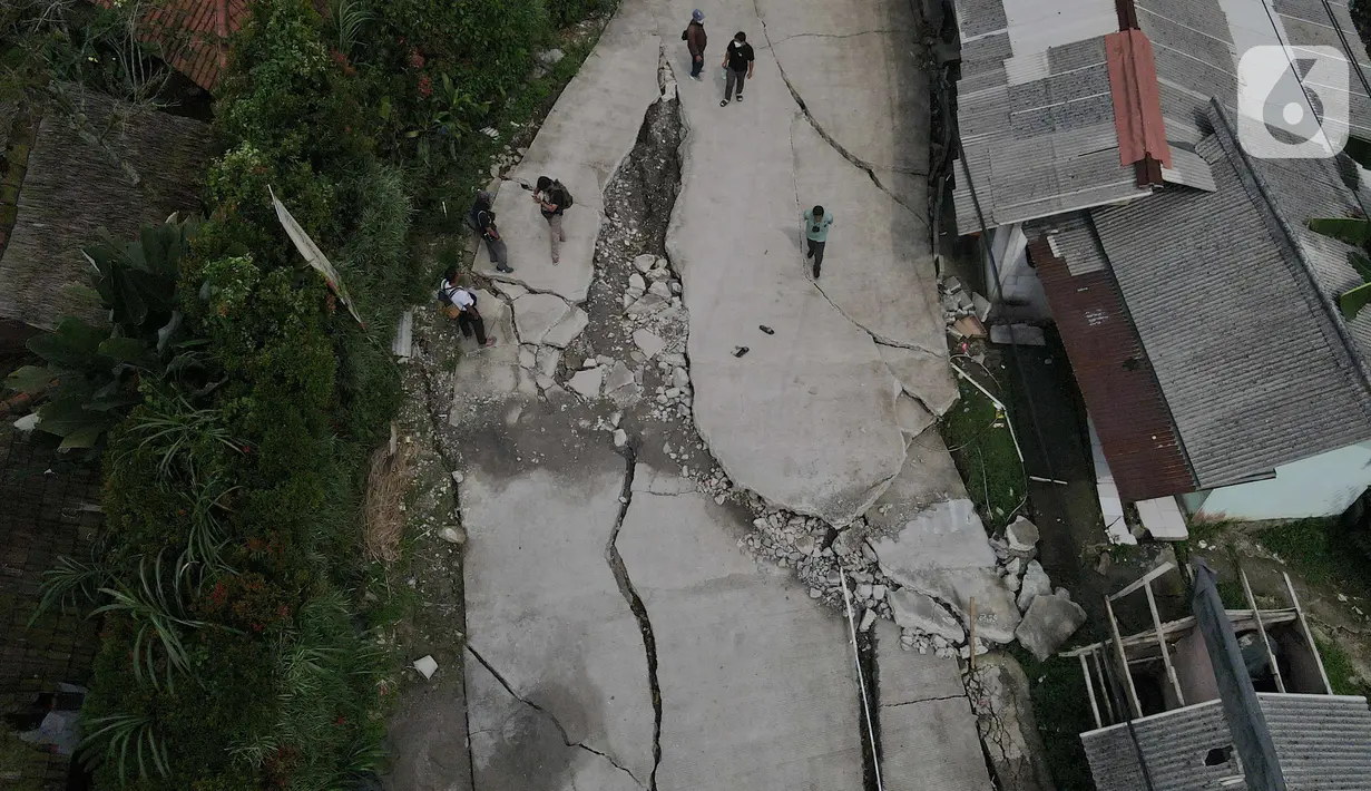 Foto udara kondisi jalan yang terbelah akibat pergeseran tanah di kawasan Bojong Koneng, Babakan Madang, Kabupaten Bogor, Jawa Barat, Jumat (16/9/2022). Badan Penanggulangan Bencana Daerah (BPBD) setempat mencatat 18 unit rumah mengalami kerusakan, dan pergeseran tanah itu menyebabkan retakan-retakan di tanah, dinding, plafon dan lantai rumah warga serta akses jalan sudah tidak bisa dilewati oleh kendaraan roda dua dan roda empat. (Liputan6.com/Herman Zakharia)