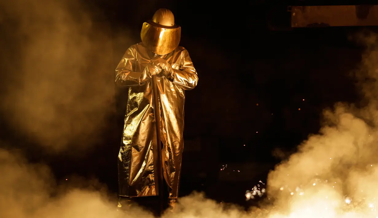 Seorang pekerja mengenakan pakaian pelindung saat berada di tungku untuk membuat baja di Salzgitter, Jerman (22/3). Karena pantulan api baju pelindung pekerja jadi terlihat berwarna keemasan. (AP Photo / Markus Schreiber)