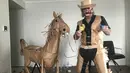 David Marriott berpose dengan kuda kertasnya Russell di kamar hotelnya di Brisbane, Australia, 1 April 2021. Direktur seni di iklan TV itu juga membuat pakaian koboi, celana topi dan juga rompi kantong kertas makanannya yang dikirimkan selama menjalani karantina. (David Marriott via AP)