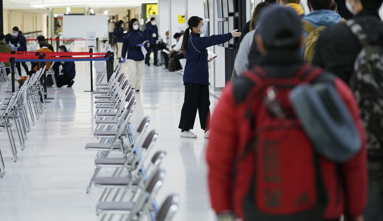 Seorang staf mengarahkan penumpang untuk duduk dan menunggu giliran selama proses karantina pencegahan virus corona setelah mendarat di Bandara Internasional Narita di Narita, timur Tokyo, Jepang (2/12/2021). (AP Photo/Hiro Komae)