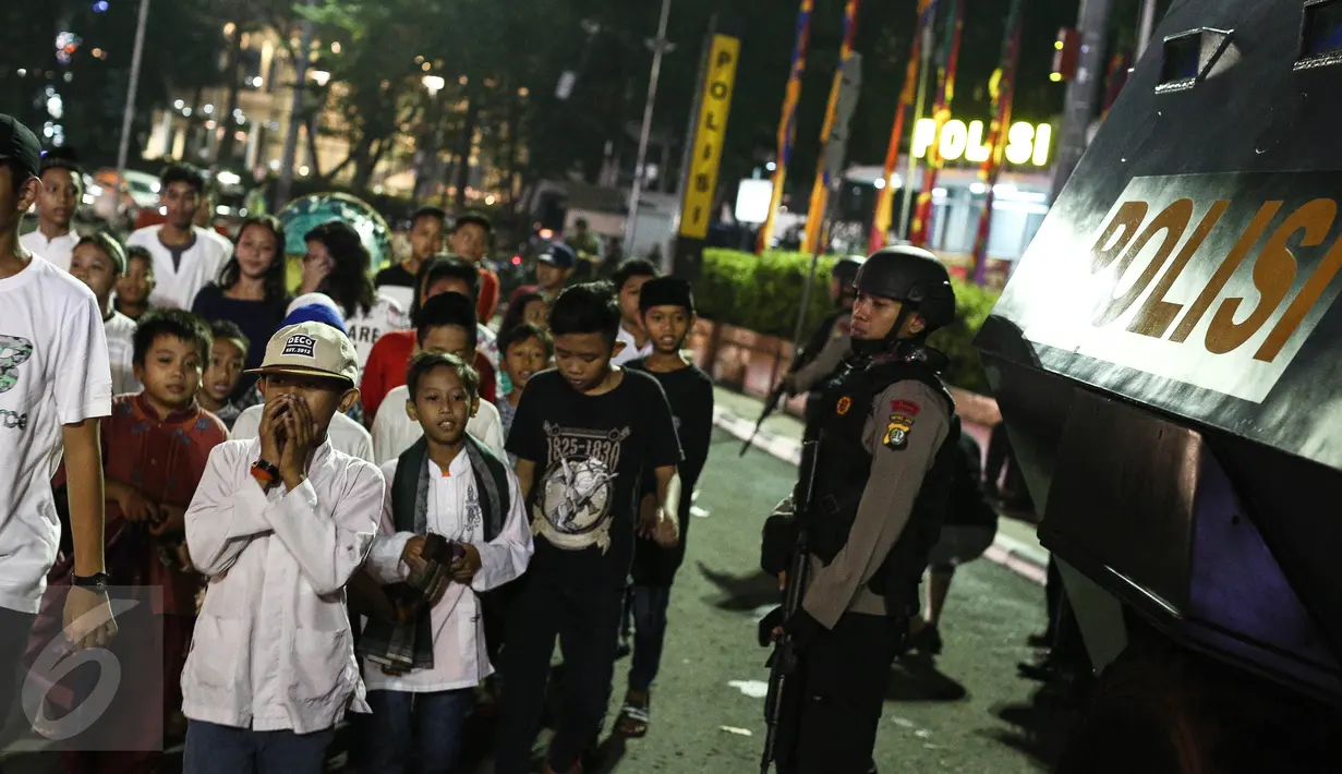 Warga yang sedang takbiran melintas didepan petugas Brimob yang berjaga-jaga dikawasan Bunderan HI, Jakarta, Selasa (6/7). (Liputan6.com/Faizal Fanani)