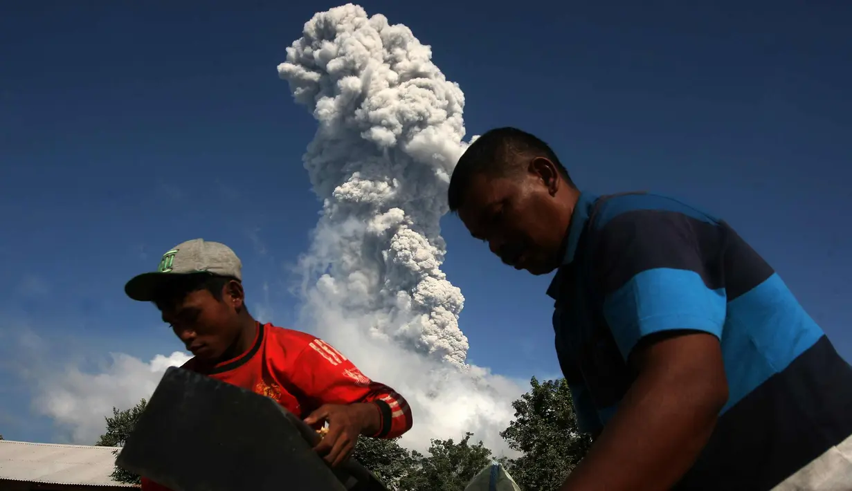 Warga beraktivitas di tengah erupsi Gunung Sinabung yang kembali memuntahkan asap dan abu vukanik ke udara di Karo, Sumatera Utara, (18/1). Aktivitas Gunung Sinabung terus mengalami peningkatan. (AFP Photo/YT Haryono)