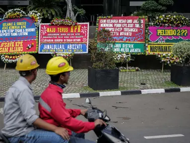 Pengendara melintas di depan karangan bunga berisi dukungan pada KPK di Gedung KPK, Jakarta, Senin (20/11). Karangan bunga tersebut sebagai bentuk dukungan masyarakat kepada KPK terhadap pemberantasan kasus korupsi e-KTP. (Liputan6.com/Faizal Fanani)