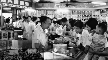 Pekerja melayani pelanggan di sebuah toko kue selama jam sibuk di Shanghai, China pada 24 September 1974. (AFP Photo)