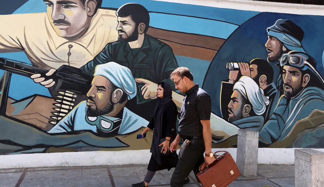 Pejalan kaki melewati mural yang menggambarkan sejumlah pria dengan senjata di Palestine Square, Ibu Kota Teheran, Iran, Sabtu (22/6/2019). (ATTA KENARE/AFP)