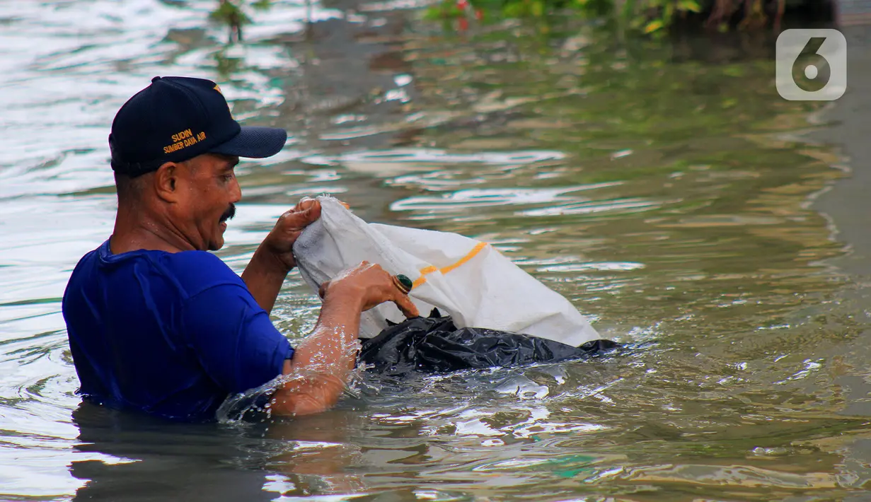 Petugas Sudin Sumber Daya Air (SDA) memunguti sampah-sampah yang tergenang saat banjir di kawasan Kampung Melayu Kecil, Bukit Duri, Jakarta, Selasa (25/2/2020). Banjir tersebut akibat luapan sungai Ciliwung. (merdeka.com/magang/ Muhammad Fayyadh)