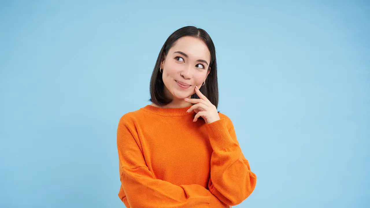 Seorang perempuan berbaju oranye sedang berpikir sambil memegang pipinya menggunakan telunjuk (Foto Dok: Freepik/benzoix)