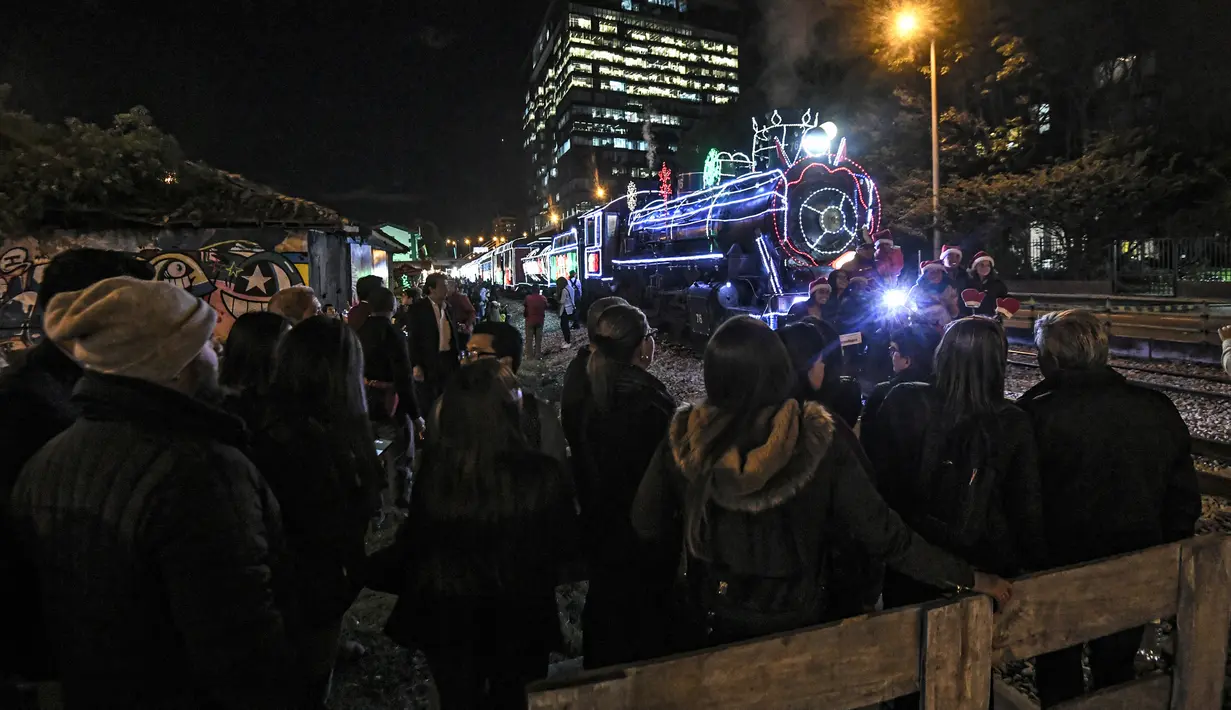 Sejumlah penumpang berpose di depan kereta wisata yang dihiasi lampu Natal di Bogota (20/12/2019). Meyambut Hari Natal, kereta wisata di Kolombia membuat cara unik dengan memasangkan lampu warna-warni agar menjadi daya tarik penumpang. (AFP Photo/Juan Barreto)