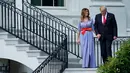 Presiden AS Donald Trump menggandeng tangan Melania sambil menuruni tangga menyambut keluarga militer pada acara piknik di Gedung Putih, Rabu (4/7). Pasangan yang jarang bergandengan di depan umum itu langsung mencuri perhatian. (AFP/Brendan Smialowski)