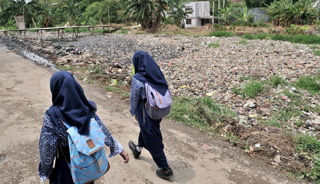 Anak sekolah melintas di pinggir Kali Pisang Batu yang dipenuhi sampah, Tarumajaya, Bekasi, Jawa Barat, Rabu (9/1). Warga tetap beraktivitas meski bau tak sedap menghantui mereka akibat tumpukan sampah di kali tersebut. (Merdeka.com/Iqbal S. Nugroho)