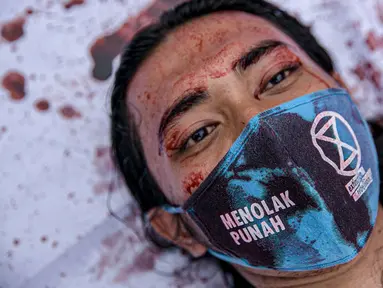 Aktivis melakukan teatrikal dengan menyiramkan darah di tubuhnya saat aksi serentak desak Presiden Jokowi deklarasikan Darurat Iklim di kawasan Patung Kuda, Jakarta, Jumat (19/3/2021). Aksi ini sebagai simbol banyaknya bencana yang terjadi di Indonesia. (Liputan6.com/Faizal Fanani)
