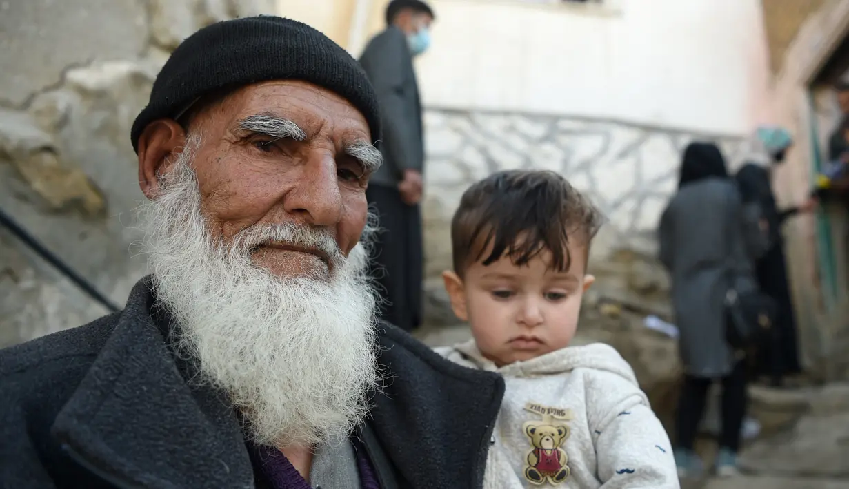 Seorang pria menggendong seorang anak saat petugas kesehatan (kanan atas) memberikan vaksin polio selama kampanye vaksinasi di kawasan tua Kabul, Afghanistan pada 8 November 2021. Vaksinasi tersebut merupakan yang pertama sejak Taliban berkuasa di Afghanistan. (WAKIL KOHSAR / AFP)
