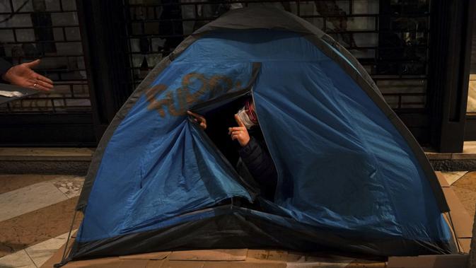 Seorang tunawisma berbicara dari dalam tendanya saat pembagian makanan gratis di pusat kota Milan, Italia utara, 27 November 2020. Tidak ada tempat di Italia yang kemiskinan lebih jelas daripada di Lombardy, wilayah utara yang sempat menjadi episentrum penularan COVID-19. (AP Photo/Luca Bruno)
