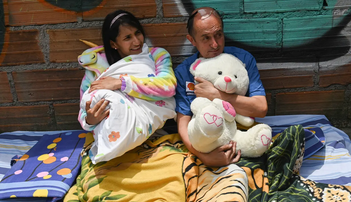 Sepasang suami istri berbaring di lantai ketika orang-orang berparade merayakan Hari Malas Sedunia di Itagui, dekat Medellin, Kolombia, Minggu (18/8/2019). (JOAQUIN SARMIENTO/AFP)
