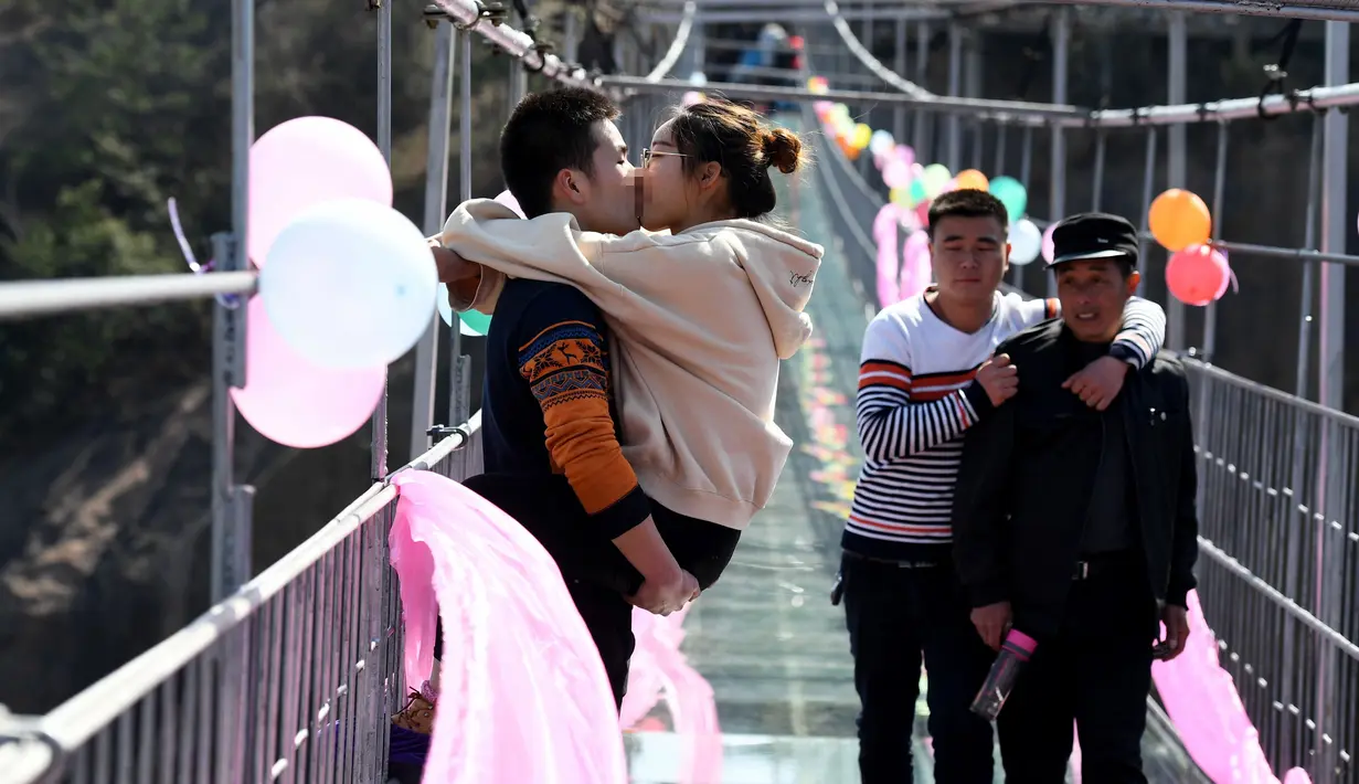 Dua orang pria memperhatikan kontestan yang sedang berciuman diatas sebuah jembatan kaca di Pingjiang, Provinsi Hunan, China (14/2). Kontes ini digelar untuk merayakan hari valentine yang jatuh pada setiap tanggal 14 Februari. (STR / AFP)