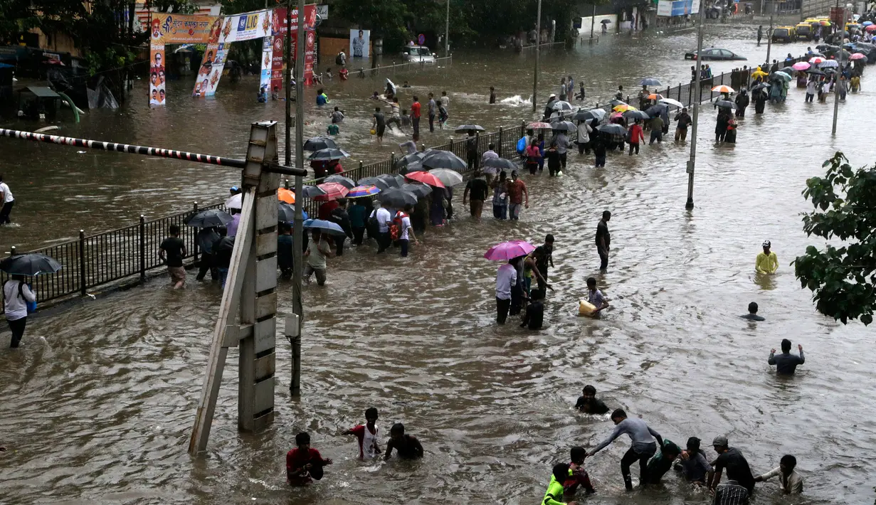 Sejumlah orang berjalan menerobos banjir akibat hujan lebat mengguyur kota Mumbai di India, Selasa (29/8). Banjir dan buruknya cuaca juga membuat penerbangan dialihkan dan perjalanan kereta api lokal terhambat. (AP Photo/Rajanish Kakade)