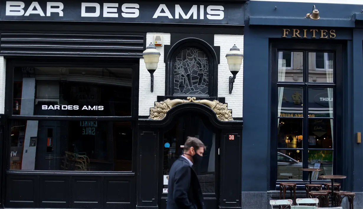 Seseorang berjalan melewati bar yang tutup pada hari kembali diperketatnya pembatasan sosial di Brussel, Belgia, Kamis (8/10/2020). Brussels pada Rabu (7/10), memutuskan menutup semua bar, ruang dansa, dan kafetaria selama sebulan sebagai upaya membendung lonjakan COVID-19. (Kenzo TRIBOUILLARD/AFP)