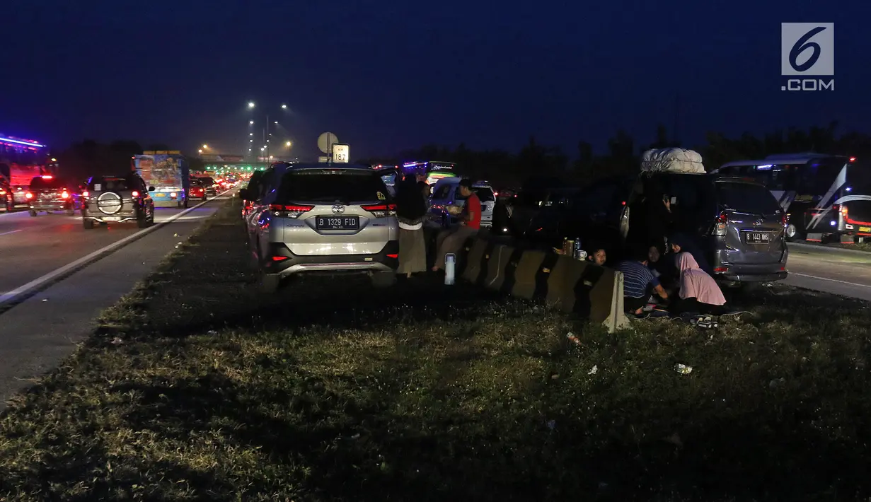Pemudik beristirahat sembari menyantap makanan untuk berbuka puasa di pinggir ruas jalan tol Cipali KM 187, Kabupaten Cirebon, Jawa Barat, Kamis (30/5/2019). Sejumlah pemudik memilih menggunakan bahu jalan ruas tol untuk berbuka puasa karena penuhnya rest area. (Liputan6.com/Herman Zakharia)