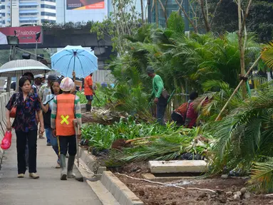 Pejalan kaki melintas saat pekerja menanam pohon di jalur pedestrian Jalan Sudirman, Jakarta, Jumat (6/7). Penanaman pohon dilakukan untuk mempercantik Jakarta jelang Asian Games 2018. (Liputan6.com/Arya Manggala)