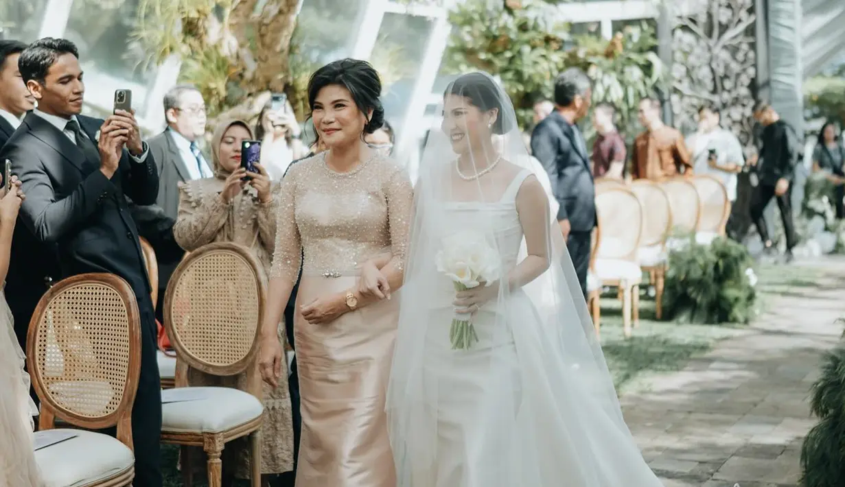 Berjalan menuju altar pernikahan, Mitzi Abigail ditemani sang ibunda sembari pamer senyuman manisnya kepada para tamu undangan. Kebahagiaan Mitzi turut dirasakan oleh netizen karena ikut mengkawal perjalanan cinta Mitzi dan Anthony Ginting selama 10 tahun ini. Aksesori berupa cincin dan kalung membuat penampilan istri Anthony Ginting ini makin cantik. (Liputan6.com/IG/@sinisukanthony)