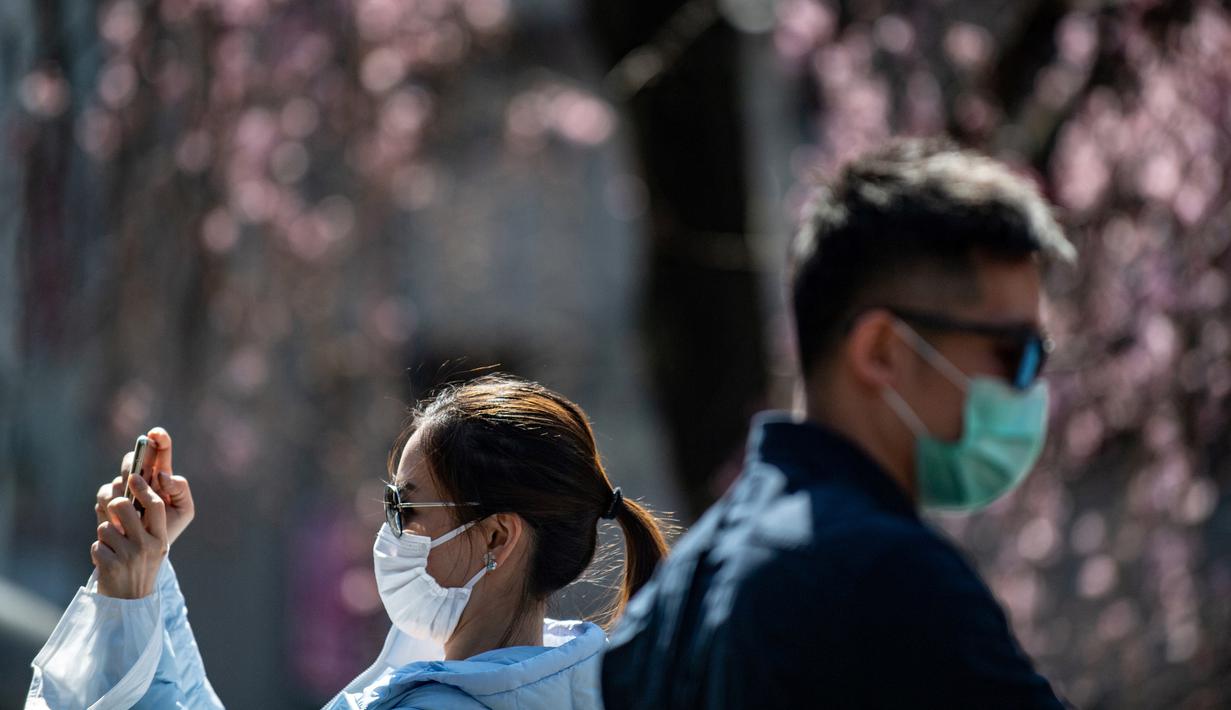 Seorang wanita mengenakan masker melewati pohon sakura di taman Ueno, Tokyo, Jepang (12/3/2020).  Di tengah kekhawatiran akan penyebaran virus corona COVID-19, Ahli meteorologi memprediksi bunga sakura mulai mekar sekitar 17 Maret di Tokyo.  (AFP/Philip Fong)