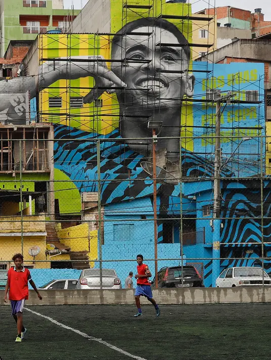 Aksi anak-anak saat bermain sepak bola di sebuah lapangan di Jardim Peri, Sao Paulo, Brasil, Minggu (20/5). Sebuah mural raksasa bergambar pemain sepak bola profesional Gabriel Jesus menghiasi permukiman mereka. (AP Photo/Andre Penner)