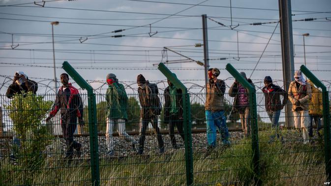 Para migran gelap yang bersiap 'menumpang' kereta dengan menyebrangi pagar. (AFP)