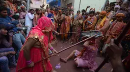 Pria saat dipukuli para wanita dengan tongkat (lathi) selama perayaan Lathmar Holi di Barsana di Mathura, India, (24/2). Lathmar Holi adalah perayaan lokal festival Hindu Holi, biasanya beberapa hari sebelum festival Holi. (AFP Photo/Dominique Faget)