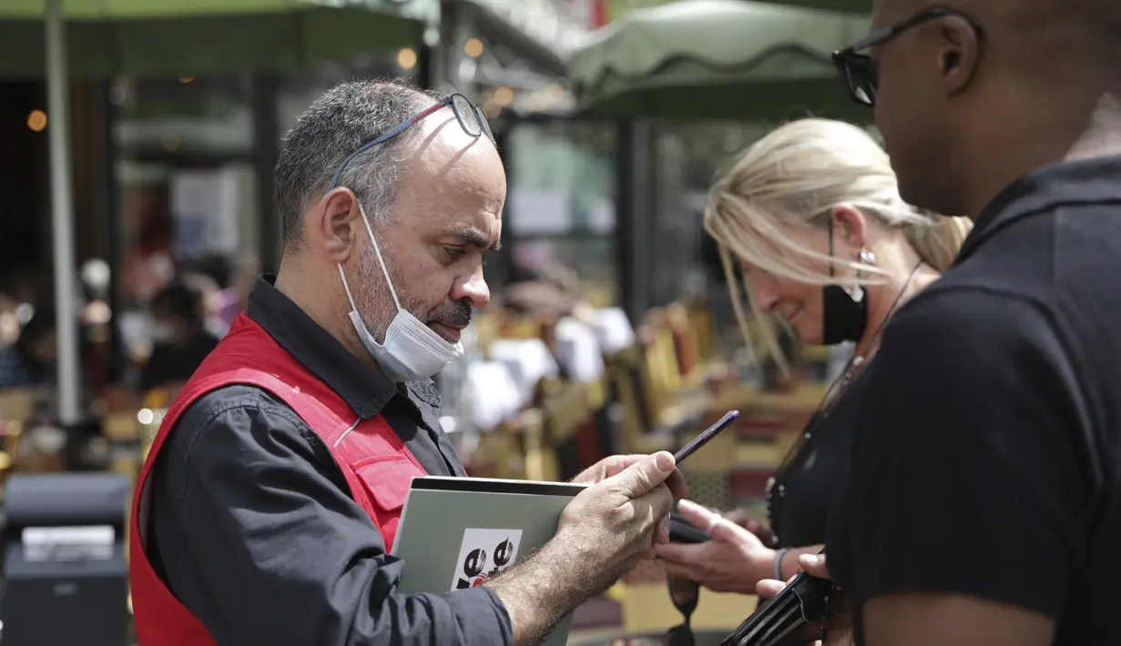 Seorang pramusaji memeriksa kartu kesehatan pengunjung di sebuah restoran di Paris, Senin (9/8/2021). Prancis mewajibkan semua orang menunjukkan kode QR yang membuktikan mereka memiliki Kartu Vaksinasi untuk memasuki restoran dan kafe atau bepergian di negara tersebut. (AP Photo/Adrienne Surprenant)