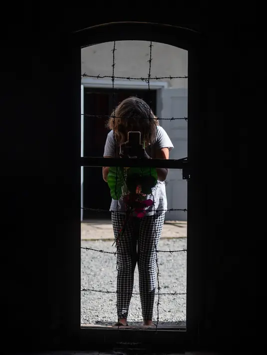 Seorang wanita mefoto di pintu masuk ke kamar gas di museum di bekas Kamp Kematian Nazi, di Sztutowo, Polandia (21/7/2020).  (AFP Photo/Wojtek Radwanski)