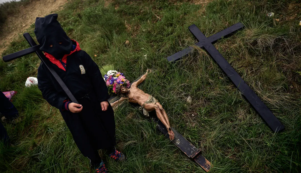 Seorang jemaat dari Ujue Virgin mengenakan topeng sambil menggendong salib saat mengikuti ziarah dari Tafalla dan desa-desa lainnya ke kota kecil Ujue, Spanyol Utara (29/4). (AP/Alvaro Barrientos)