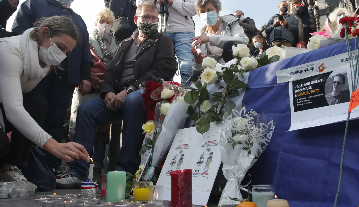 Seorang wanita menyalakan lilin di alun-alun Republique selama demonstrasi di Paris (18/10/2020). Samuel Paty dipenggal pada hari Jumat di Conflans-Sainte-Honorine oleh seorang pengungsi Chechnya. (AP Photo/Michel Euler)