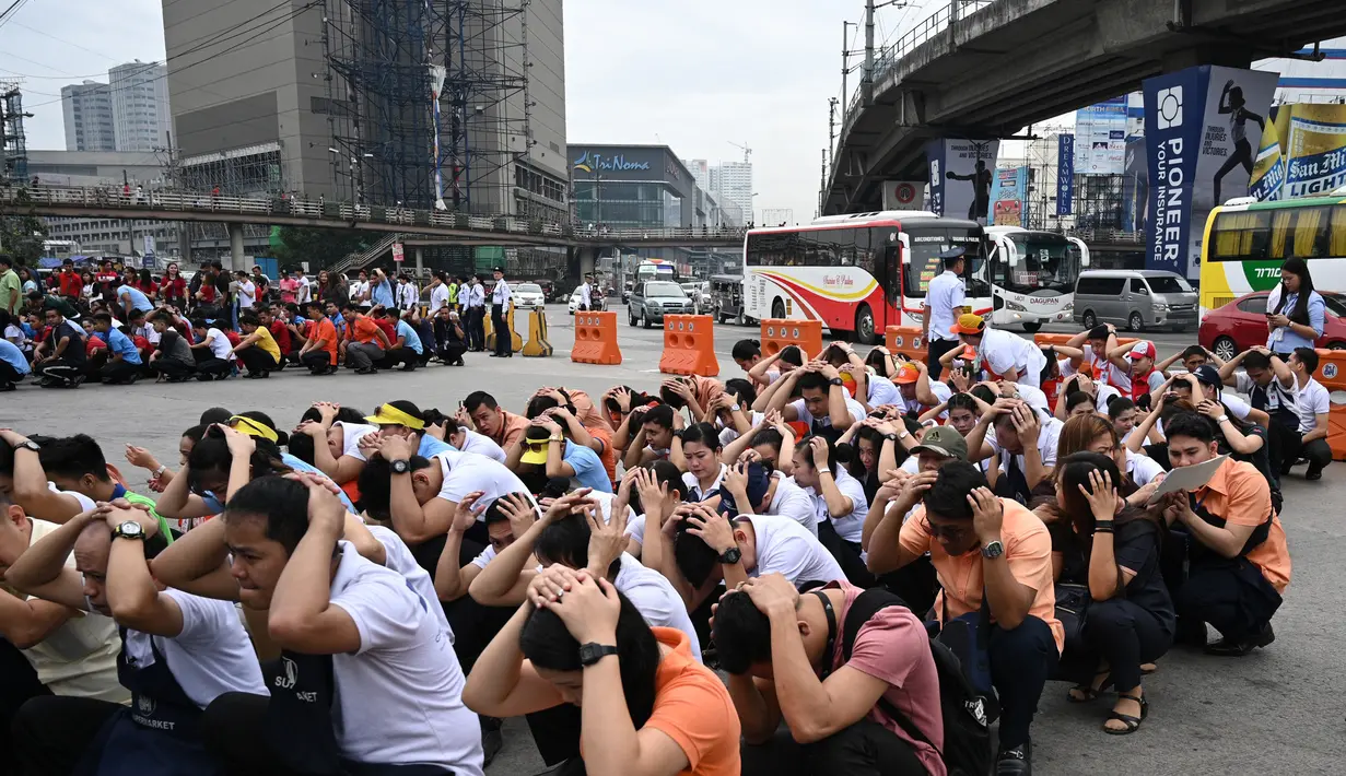 Karyawan pusat perbelanjaan menutupi kepala mereka di sepanjang jalan ketika mereka berpartisipasi dalam latihan gempa di Manila (14/11/2019). Latihan ini sebagai bagian dari kesiapsiagaan nasional menyusul berbagai gempa yang melanda pulau Mindanao bulan lalu. (AFP Photo/Ted Aljibe)